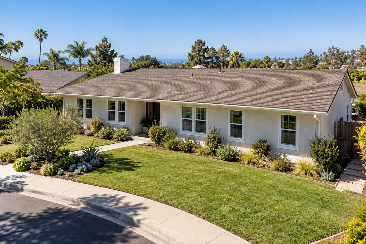 Single-story white stucco ranch home with new white double-hung windows, lawn and landscaping under a clear sky